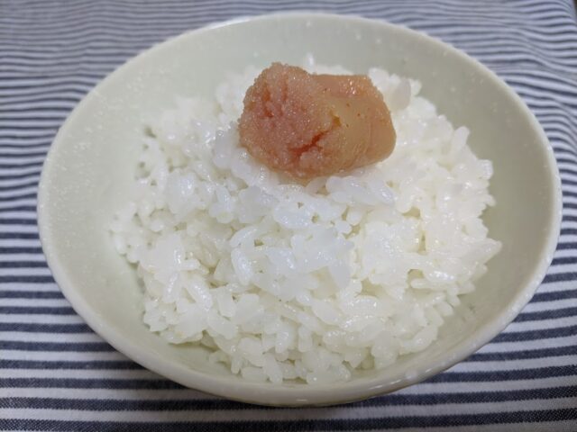 お茶碗に白ご飯を入れその上に島本のオリジナル辛子明太子をのせテーブルの上に置いている写真