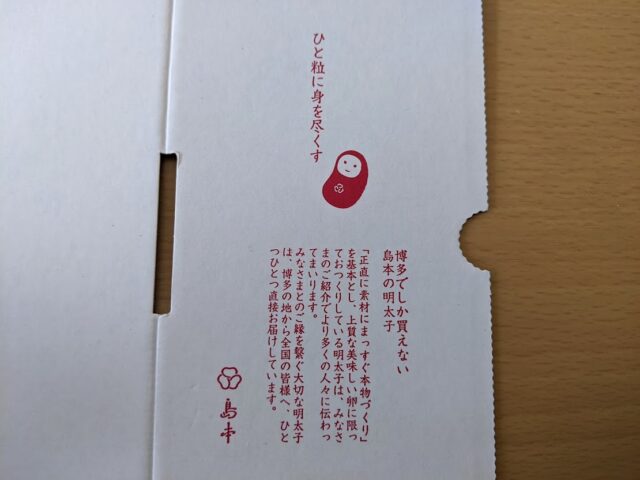島本のオリジナル辛子明太子が入っている白い箱の左に島本の明太子に対する想いがつづられている文章が写っている写真