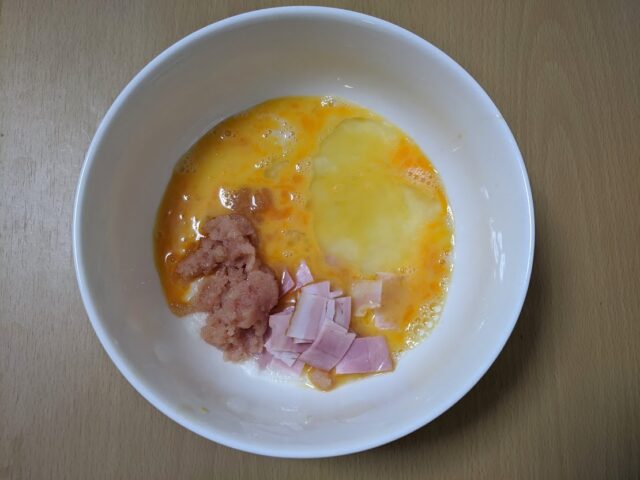 すりおろした長芋と溶き卵と島本のオリジナル辛子明太子とベーコンを合わせたものをお皿に入れテーブルに置いている写真
