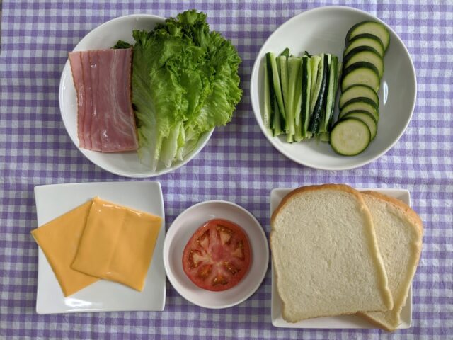 ベーコンとレタスとトマトのサンドイッチに使う材料をお皿に入れテーブルに置いている写真