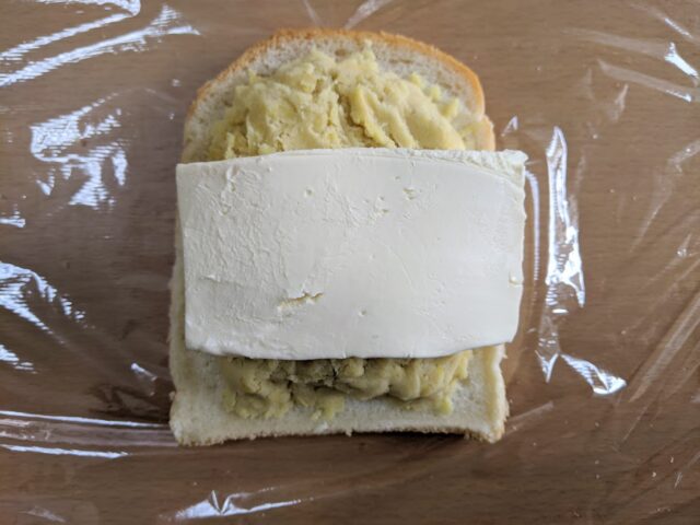テーブルにラップを敷きその上にバターをぬった食パンを置きつさつまいも餡、クリームチーズの順にのせた写真