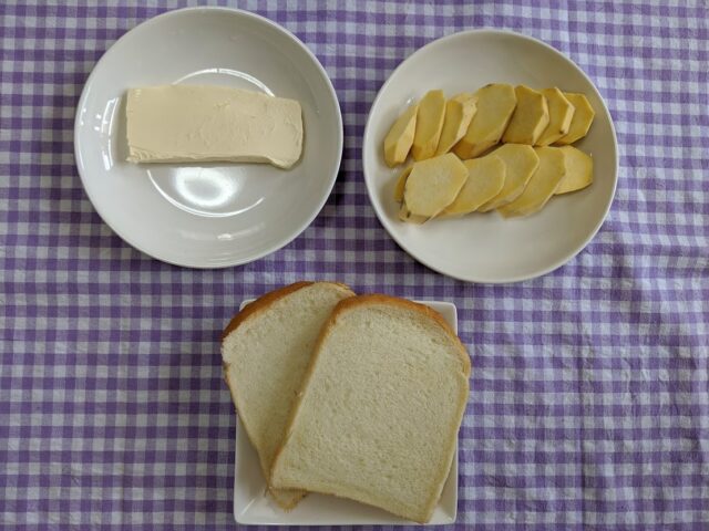 さつまいもサンドイッチに使う材料の食パンとさつまいもとクリームチーズをテーブルに置いている写真