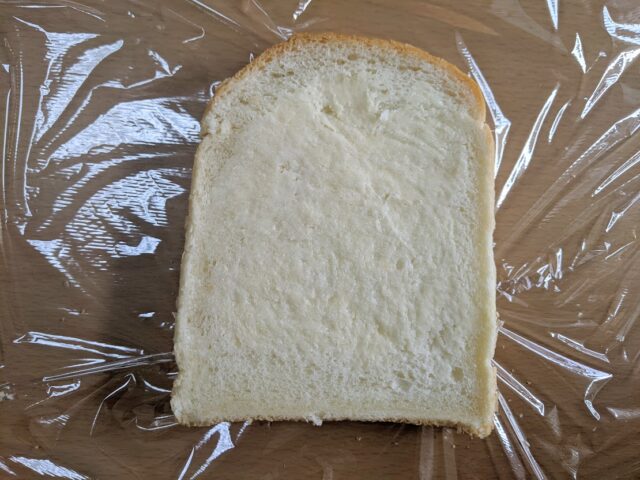 テーブルにラップを敷きその上に食パン1枚にバターをぬったものを置いている写真