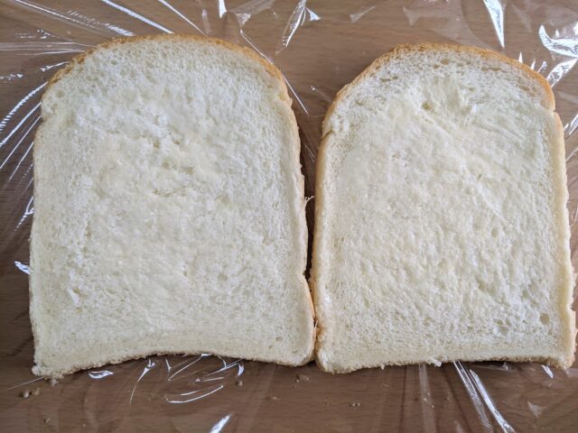 バターを食パン2枚の片面にぬったものをテーブルの上に置いている写真