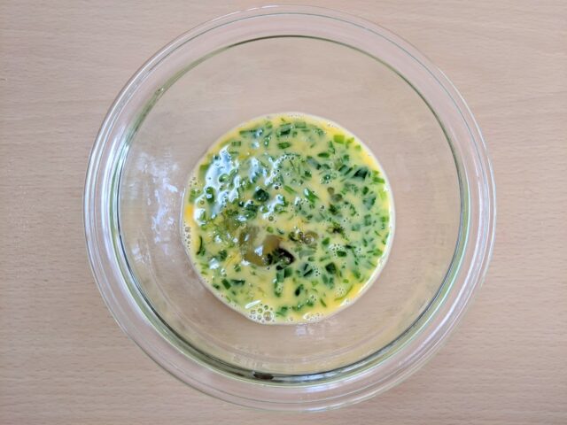 ガラスボウルに溶き卵とたまねぎの葉のみじん切りを加え混ぜたものを入れテーブルに置いている写真