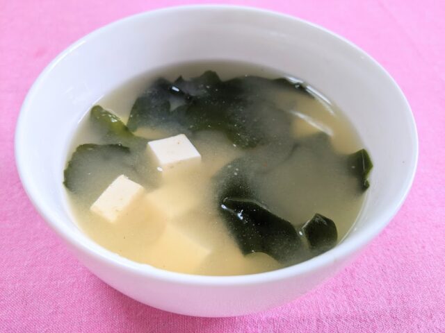 博多の味本舗の天然だしを使用したわかめと豆腐のお味噌汁一杯をお皿に入れてテーブルに置いている写真