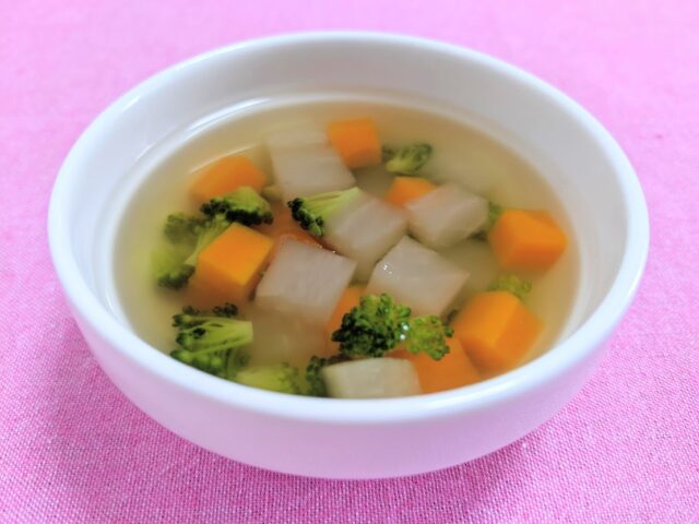 博多の味本舗「幼児期からの食育だし」を使用したにんじんとだいこんとブロッコリーの野菜スープをお皿に入れテーブルに置いている写真