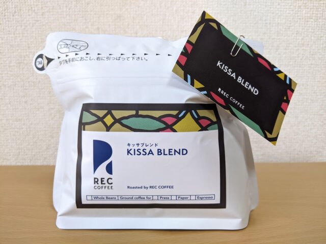 コーヒー専門店「REC COFFEE」のコーヒー豆のキッサブレンド1袋をテーブルに置いている写真