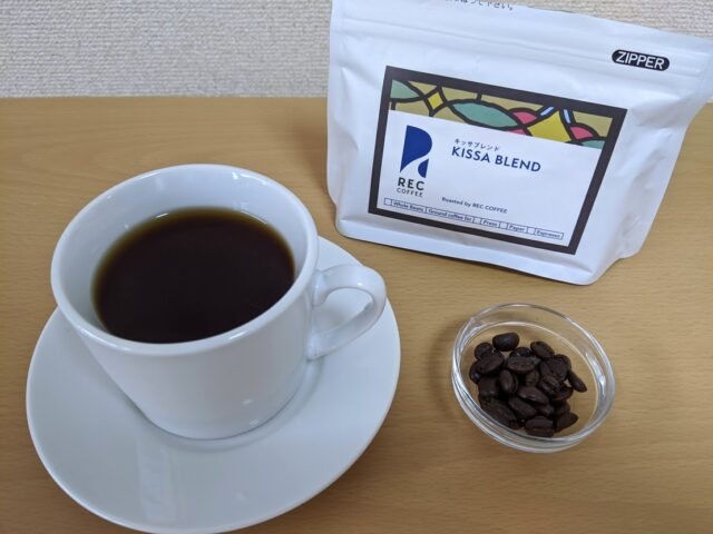 コーヒー専門店REC COFFEEのキッサブレンドのコーヒー豆とカップに入れたコーヒーをテーブルに置いた写真