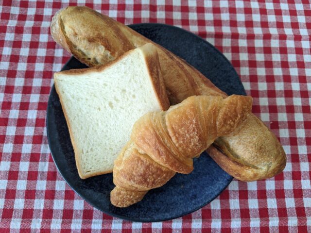 バゲットとクロワッサンと食パンをお皿にのせテーブルに置いている写真
