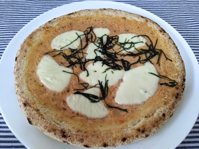 ピザ屋ピザレボの博多明太タラモ大葉の冷凍ピザをオーブンで焼いてお皿に入れテーブルに置いている写真