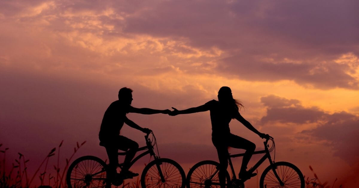 恋人が自転車に乗って手をつないでいる画像