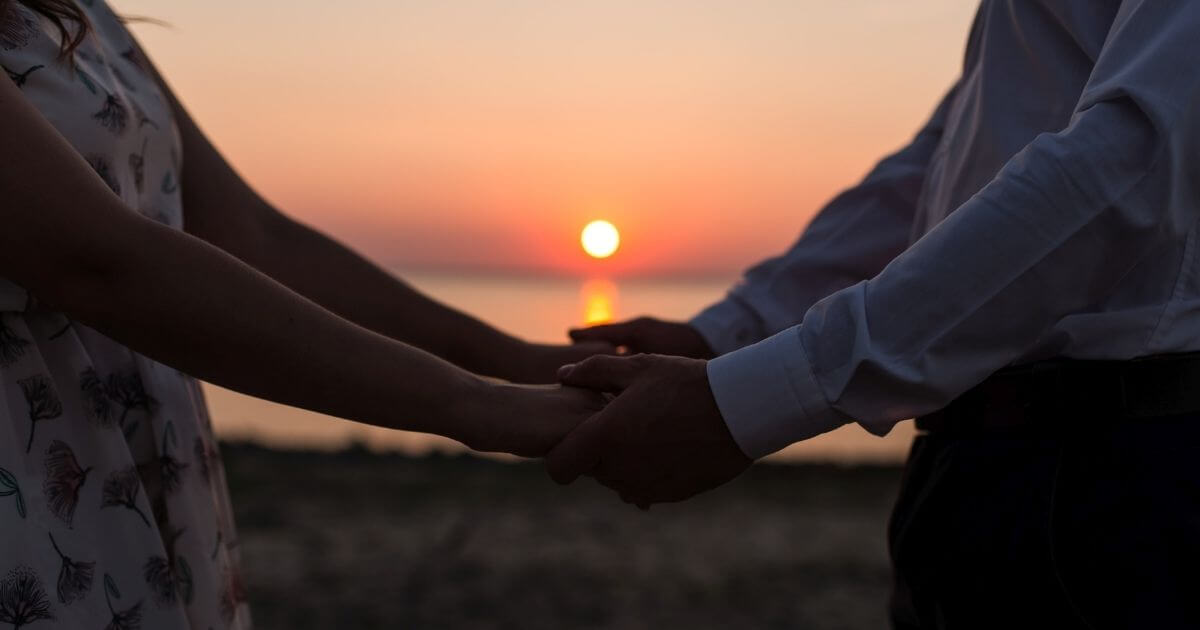 海辺の夕日が見える場所で男女が手をにつないでいる画像