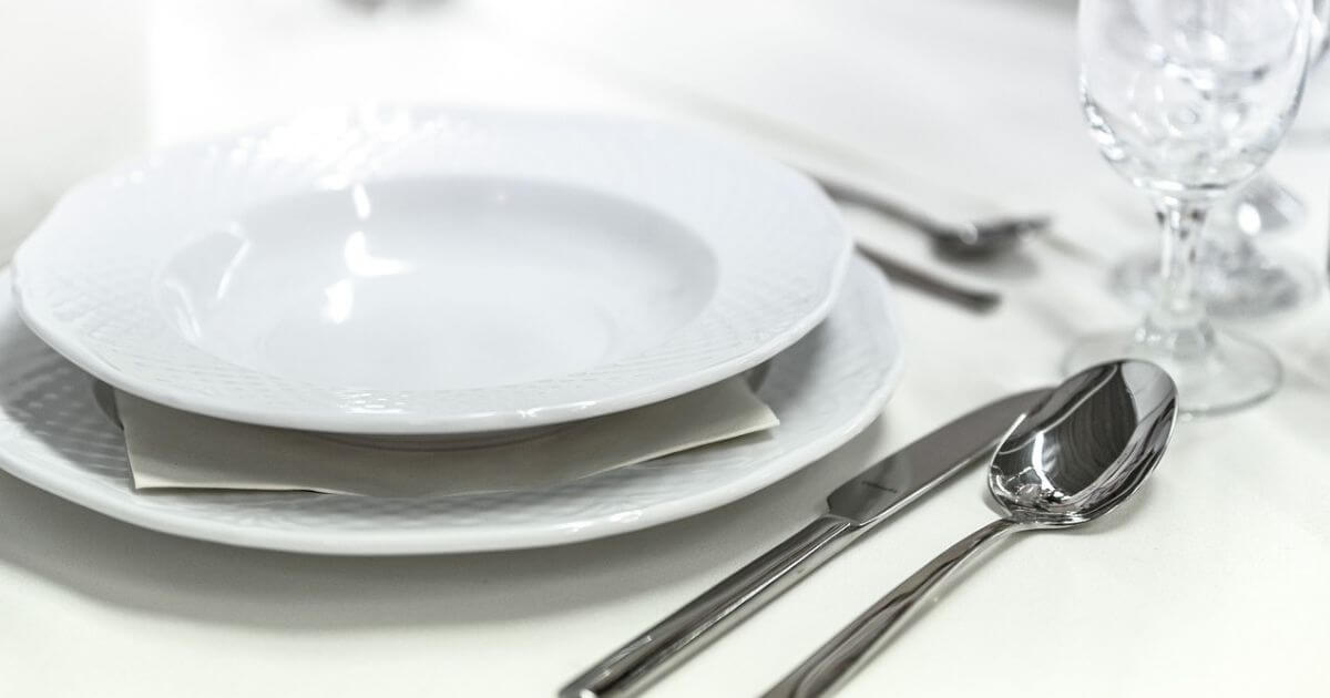 白い皿とナイフとフォークとグラスが置いてあるテーブルの画像