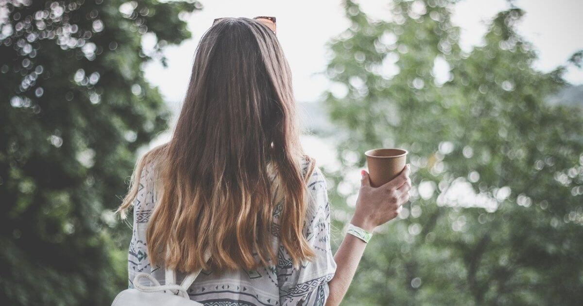 女性がコーヒーを片手に森林を眺めている後ろ姿の画像