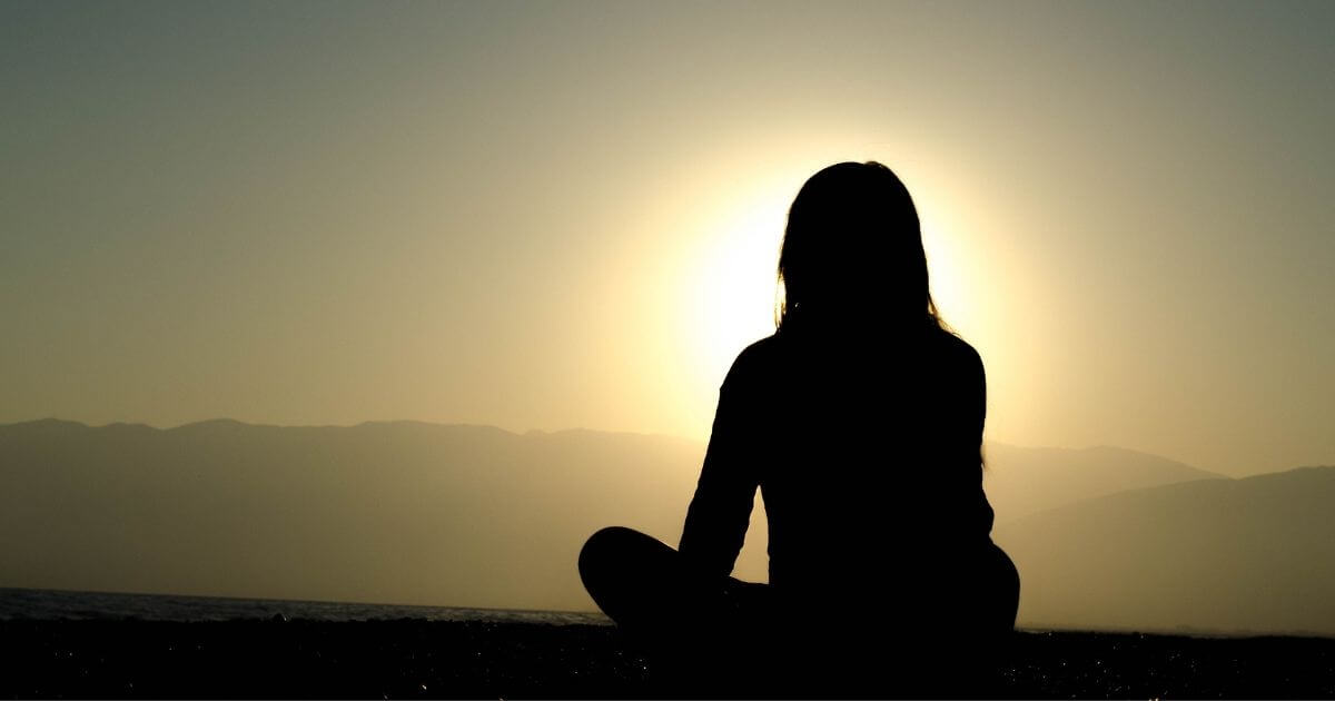 女性が夕日の光のある場所で瞑想している後ろ姿の画像