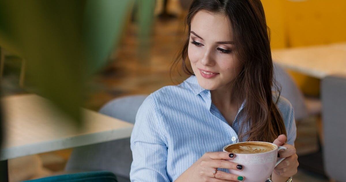 女性がカフェラテを飲みながらホッと一息ついている画像