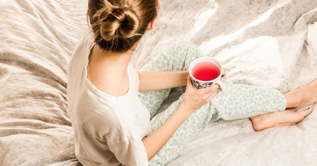 女性がベッドの上でお茶を飲んでいる画像