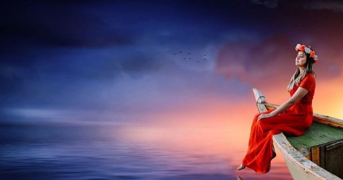 赤いワンピースを着た女性が木船の上に腰かけている画像