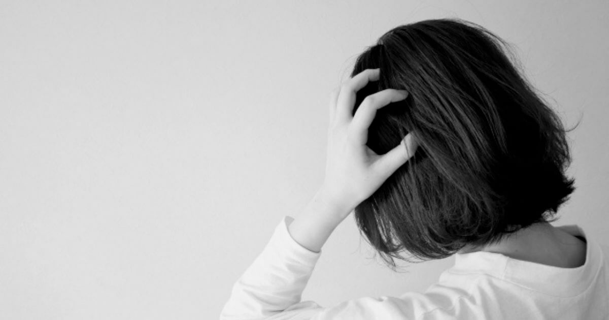 女性が両手を頭においている後ろ姿の白黒の画像