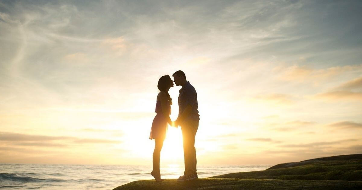 夕日の見える背景でカップルが立っている画像