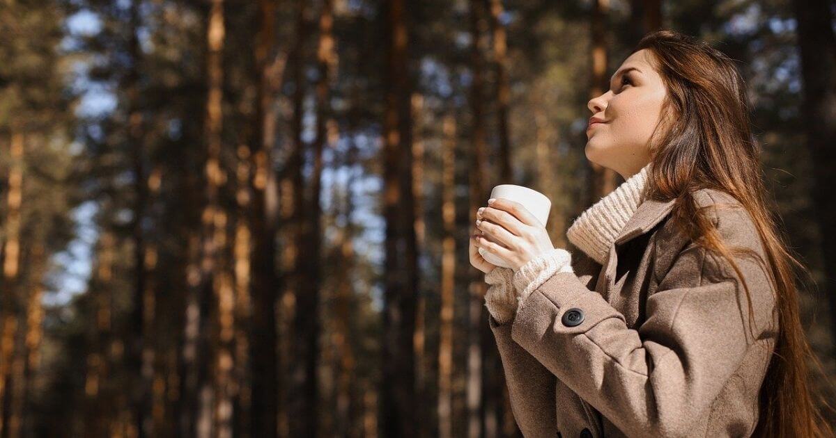 森林で女性がコーヒーカップを持ちながら空を見上げている画像