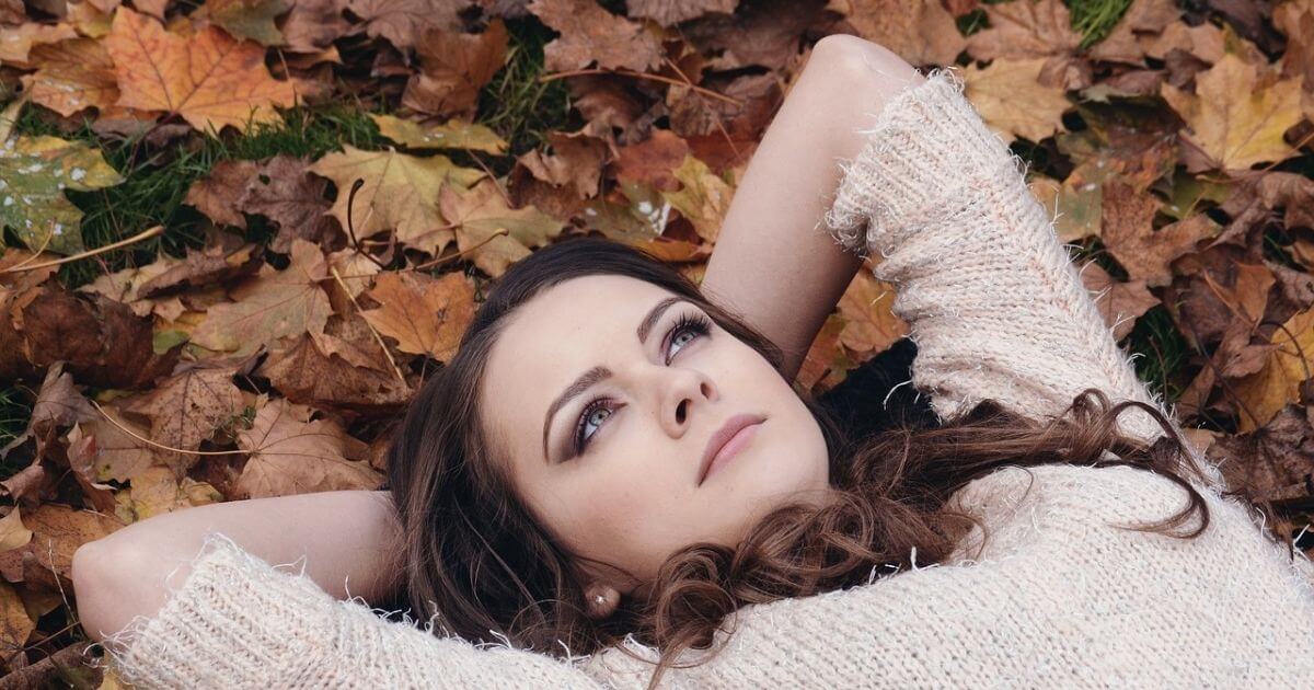 女性が枯葉の上に寝転んで空を眺めている画像