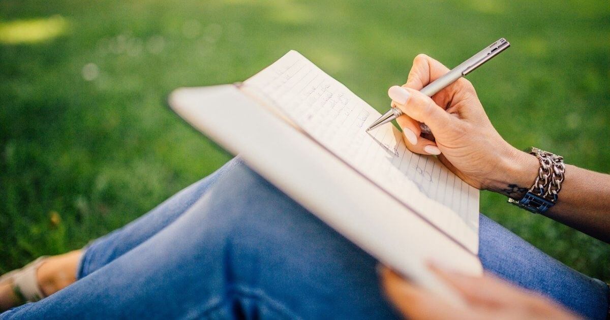 芝生の上で女性がノートを書いている画像