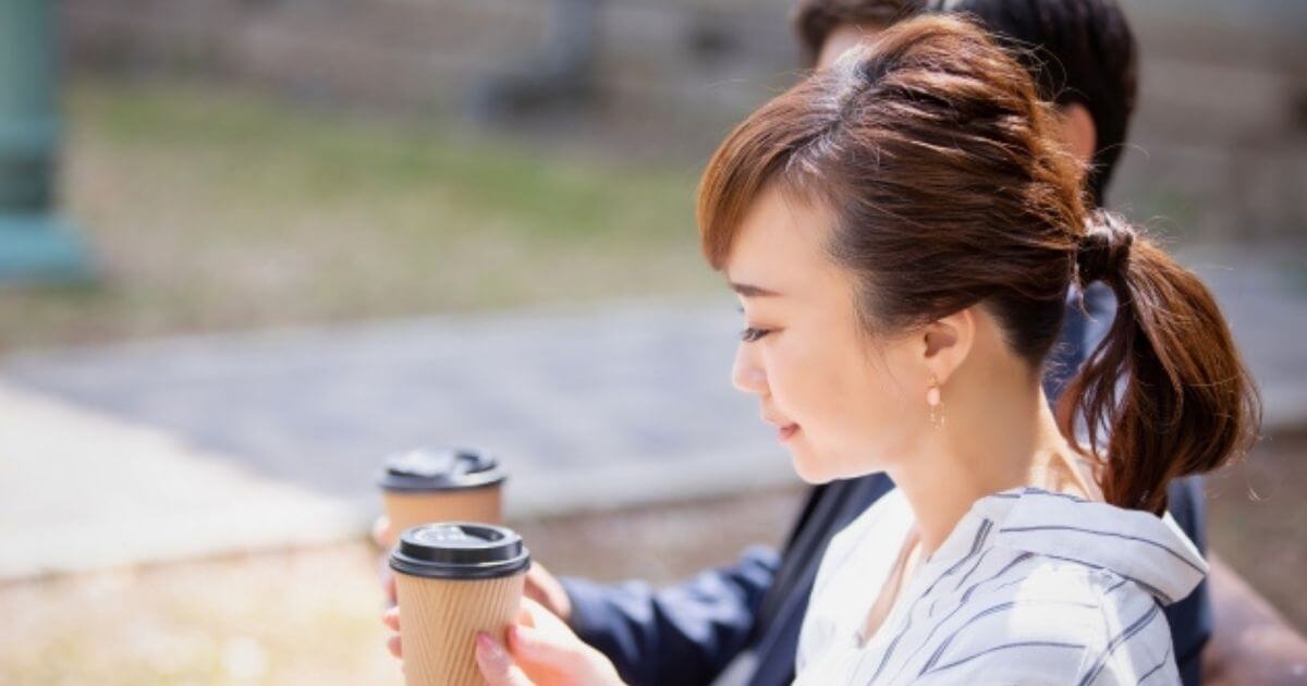 女性と男性がコーヒーを外のベンチで飲んでいる画像
